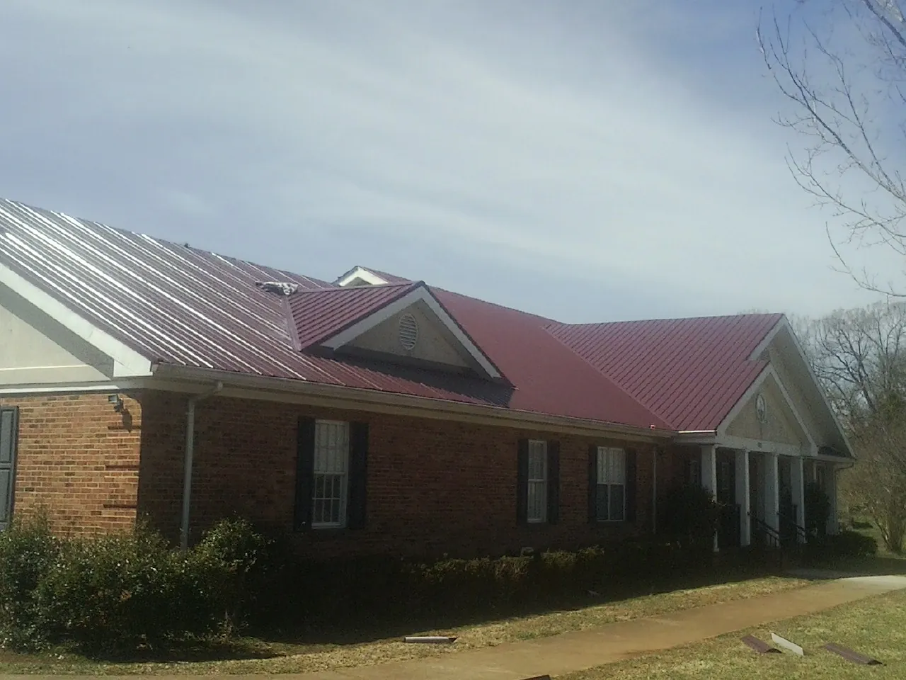 Red metal roof with gabled entries on a long brick building, from a Hail Damage Roof Repair job in Cherry Valley